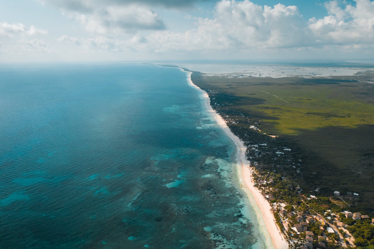 A breathtaking aerial panorama of Tulums turquoise waters and lush coastline under a bright sky.